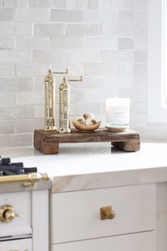 a white kitchen counter with gold accents and candles on it, next to a brick wall