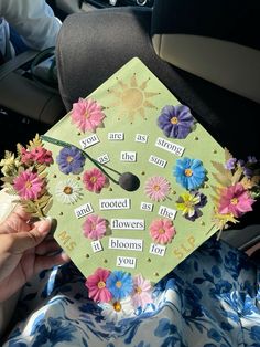 a green graduation cap with flowers and words written on the front is held in someone's hand