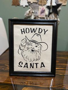 a wooden table topped with a black frame and a sign that says howdy santa