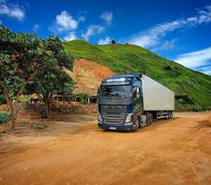 a large truck is parked in front of a green hill with trees on the side