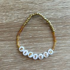 a beaded bracelet with the word fifteen spelled out in white beads on a wooden surface