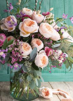 a vase filled with lots of pink flowers on top of a wooden table next to a green wall