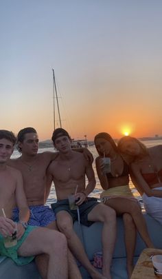 four people sitting on the back of a boat at sunset with drinks in their hands