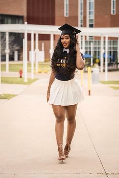 a woman in a graduation cap and skirt walks down the sidewalk with her hand on her head