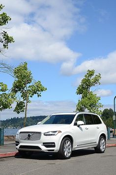 a white volvo suv parked in a parking lot next to a tree lined street with trees