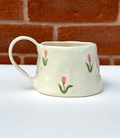 a white coffee cup with pink flowers painted on the side and green stems sticking out of it