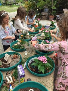 several children are looking at plants in blue buckets on a table with dirt around them