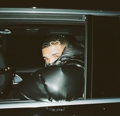 a man in black leather gloves leaning out the back door of a car at night