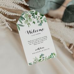 a welcome card with greenery on it sitting next to a bouquet of flowers and leaves