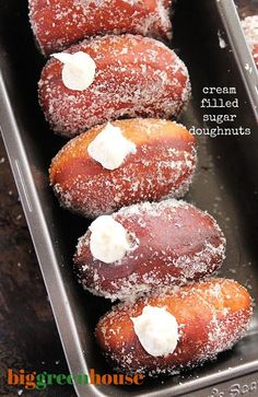 four doughnuts with cream filled sugar toppings in a metal tray on a table