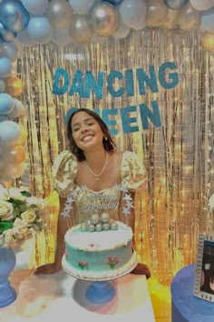 a woman sitting in front of a cake on top of a table next to balloons