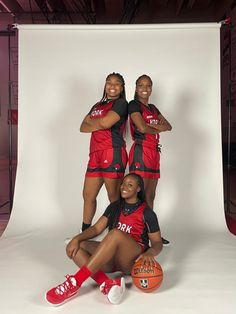 three women in red and black uniforms posing for a photo with basketballs on the floor