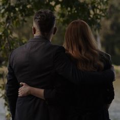 a man and woman standing next to each other in front of a body of water