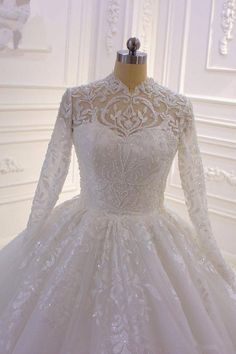 a white wedding dress with long sleeves on a mannequin head stand in front of a wall