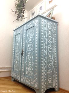 a blue cabinet with white designs on the doors and drawers is sitting in front of a plant