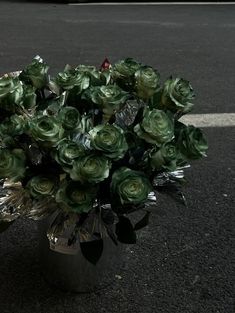 a vase filled with green flowers sitting on the side of a road next to a parking lot