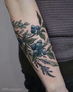 a woman's arm with an olive branch and blue berries tattoo on the left forearm