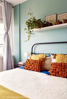 a bed with two pillows and some plants on top of the headboard in front of a window