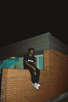 a young man sitting on top of a brick wall next to a building at night