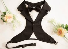 a black vest with a bow tie and some flowers on the table next to it