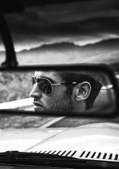 a man in sunglasses is looking at himself in the rear view mirror as he drives