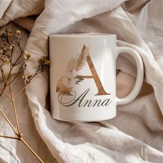 a white coffee mug sitting on top of a bed next to dried flowers and blankets