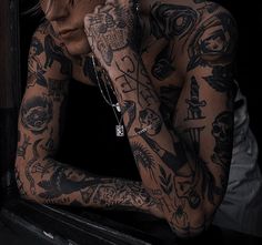 a woman with many tattoos on her body and hands behind her head, leaning against a window sill