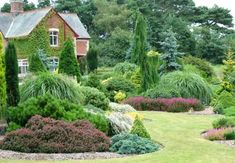 a house surrounded by lush green trees and flowers in front of it is a garden