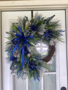 a wreath with blue and silver decorations hanging on the front door, next to a window