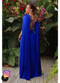 a woman wearing a blue dress standing in front of flowers and greenery with her back to the camera