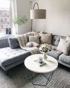 a living room with grey couches and pillows on top of the sofa, next to a large window