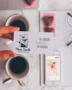 a person holding up a business card next to two cups of coffee and other items