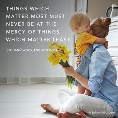 a woman sitting on the floor holding a baby and giving her a bouquet of daffodils