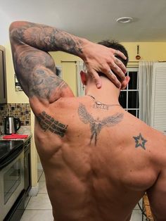 a man with tattoos on his back standing in a kitchen