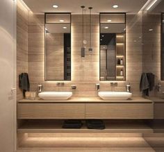 a bathroom with two sinks, mirrors and lights on the wall above them is illuminated by recessed lighting