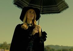 a woman holding an umbrella while standing in the sand with her hand on her hip