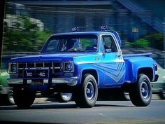 an old blue pickup truck driving down the street