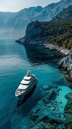 a boat floating on top of a body of water next to a rocky shore with mountains in the background