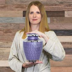 a woman holding up a purple vase in front of a wooden wall