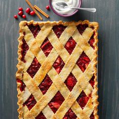 a pie with latticed crust and strawberries on the side next to a bowl of whipped cream