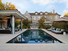 an outdoor swimming pool with lounge chairs and umbrellas in front of a large house