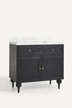 a black cabinet with white marble top and wooden legs on wheels, against a plain background