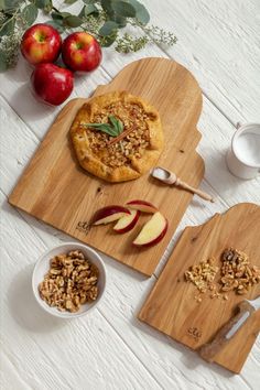 two wooden cutting boards topped with pies next to bowls of nuts and apples on a white table