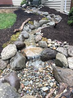 a garden with rocks and water flowing from the top to the bottom, in front of a house