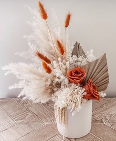 an arrangement of dried flowers in a white vase on a wooden table with a fan