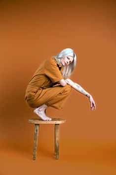 a woman sitting on top of a wooden stool with her legs crossed and one leg bent