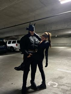 a man and woman dressed as batman and catwoman standing in an empty parking garage