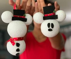 a person holding two mickey mouse ornaments in front of their face with both hands and wearing a red shirt