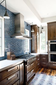 a kitchen with wooden cabinets and blue brick wall tiles on the backsplash, along with an area rug