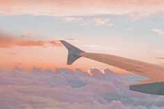 the wing of an airplane flying in the sky with clouds and pink hues behind it